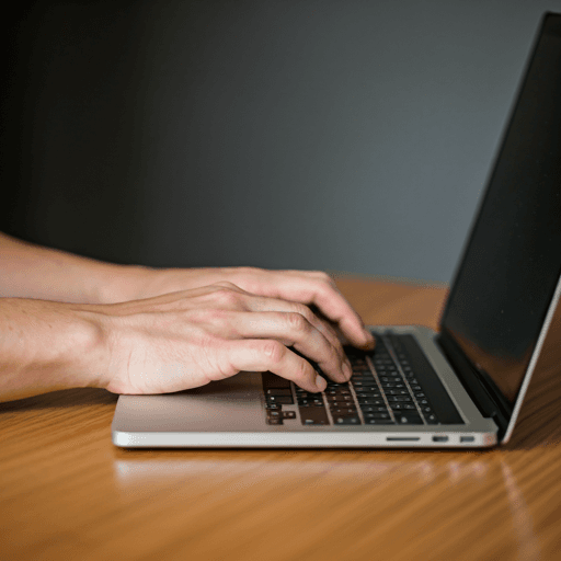 Manos escribiendo en un laptop sobre un escritorio minimalista de madera.